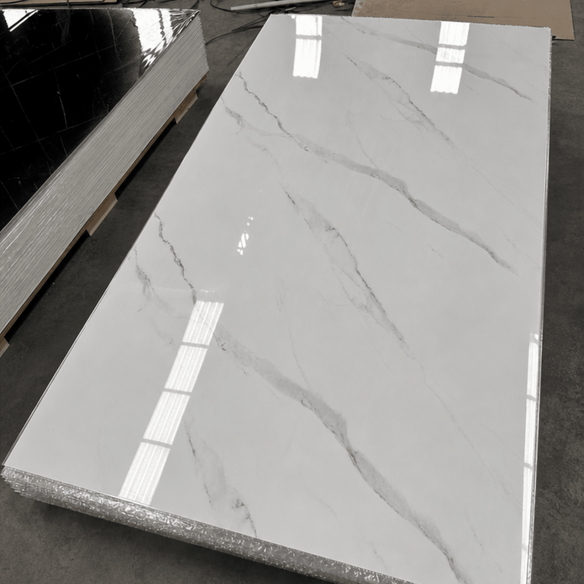 Placa PVC símil mármol blanco Carrara entera, con terminación brillante, sobre una pila de placas