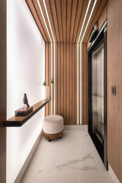 Pasillo con paredes y techo de listones de madera con luces LED, piso símil mármol y puerta negra