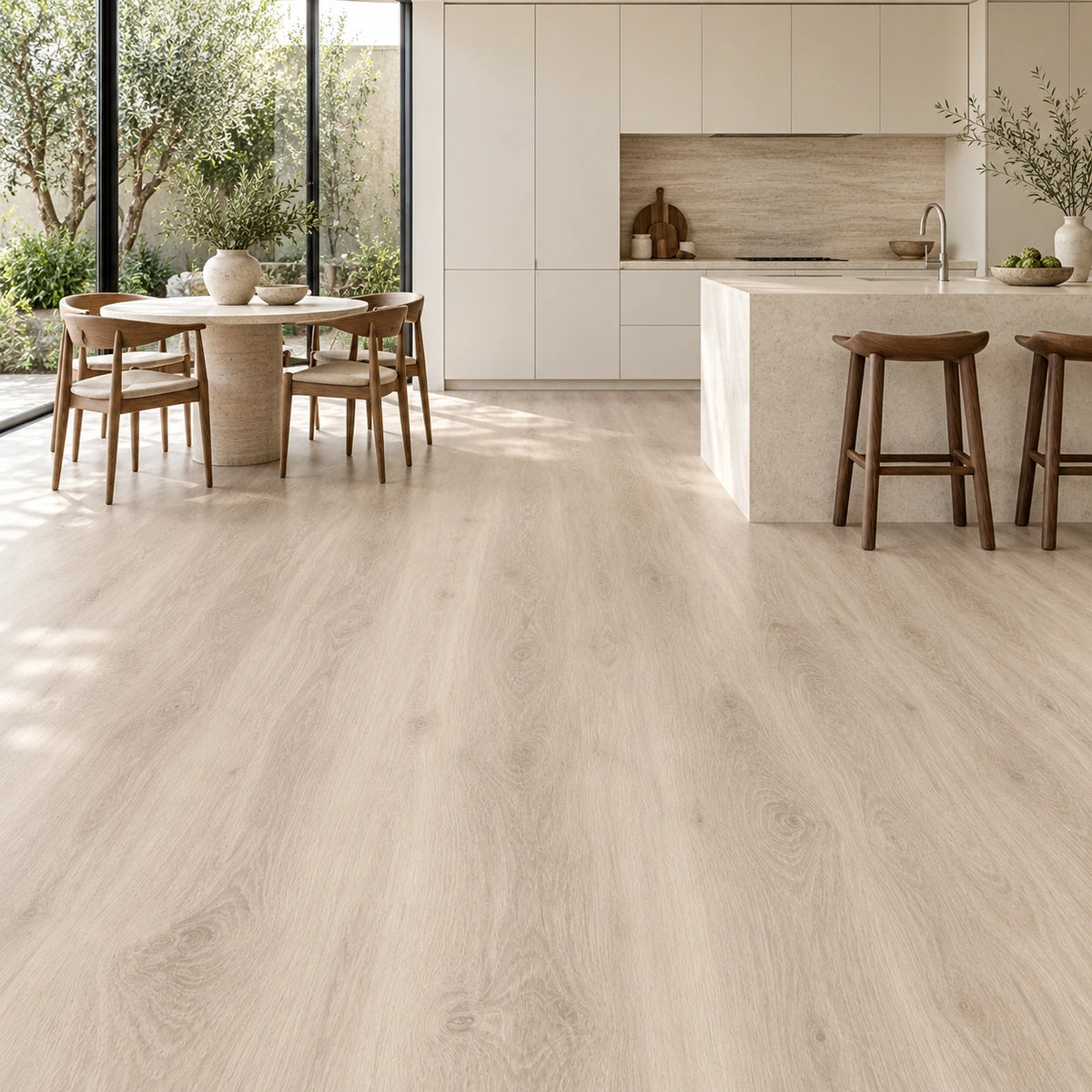 Cocina abierta con piso vinílico SPC símil roble claro, isla de piedra, banquetas de madera y comedor junto al ventanal.