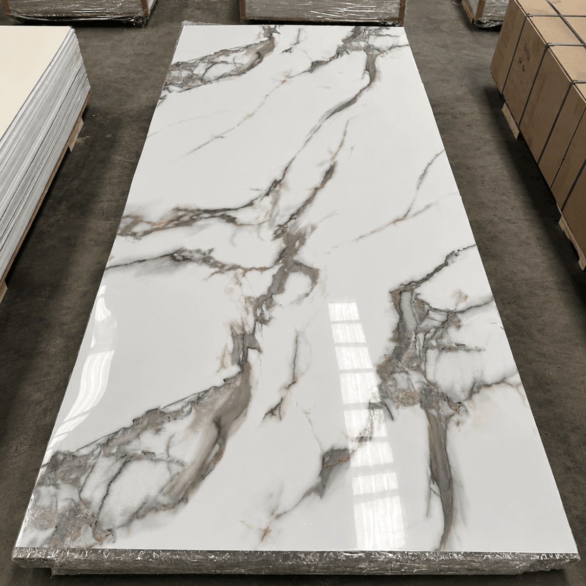 Placa PVC símil mármol blanco Calacatta entera, con terminación brillante, sobre una pila de placas